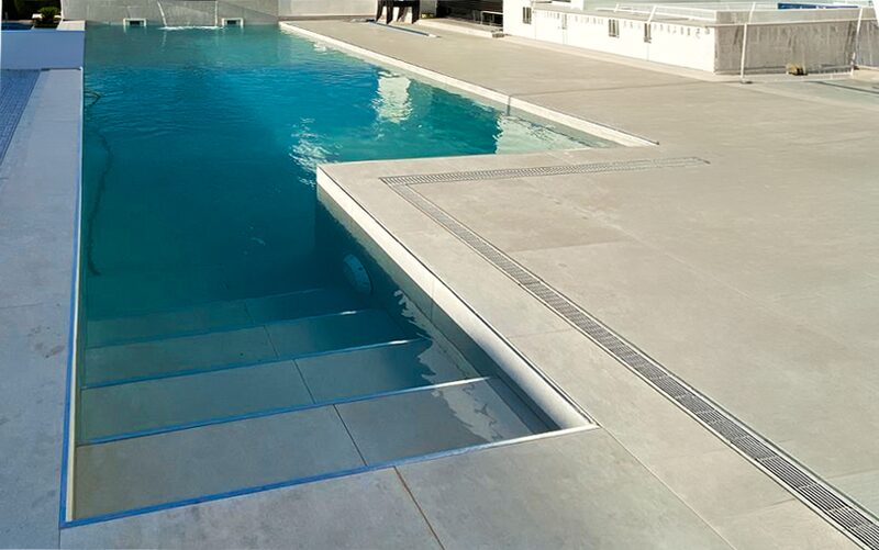 Piscina con escalera de obra ancha y rejilla perimetral en terraza de piedra gris