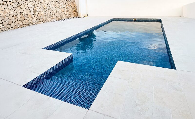 Piscina con gresite azul oscuro y playa de piedra clara junto a un muro de mampostería
