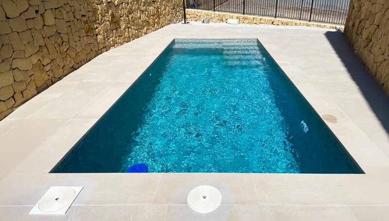 Piscina rectangular entre muros de piedra con playa color arena